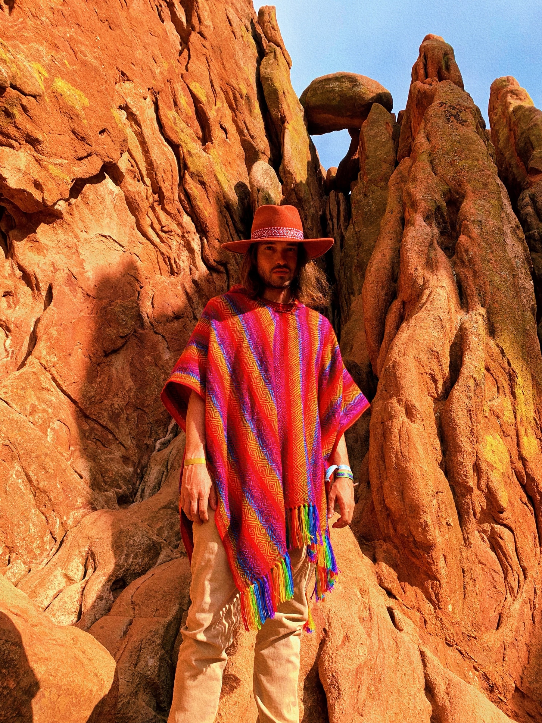 Daniel in a rainbow poncho and wide-brim hat among red rock formations
